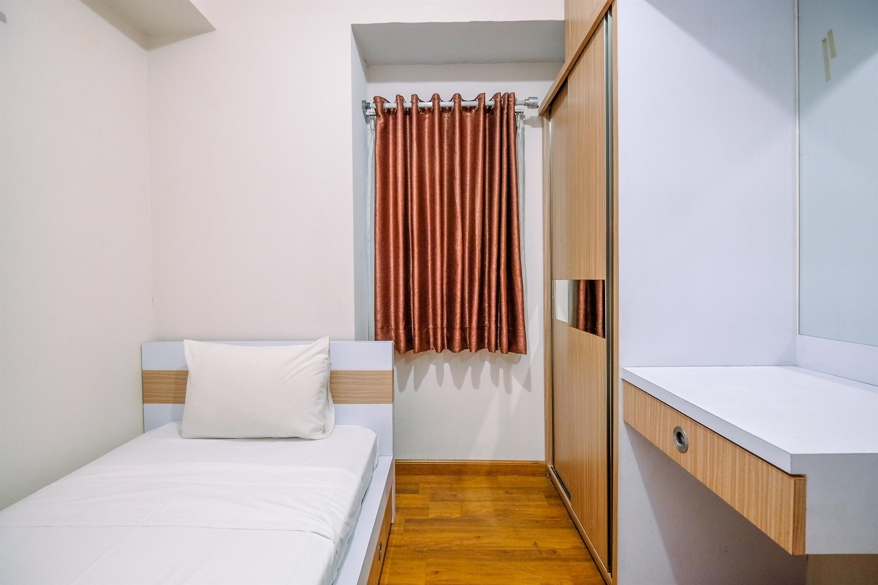 Un dormitorio pequeño y ordenado con una cama individual, un armario de madera y una zona de baño compacta.