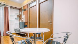 A small, modern room with a round table and two chairs, wooden cabinets, a television, and a window with curtains. - Spacious 3Br At Bogor Valley Apartment (Bogor)