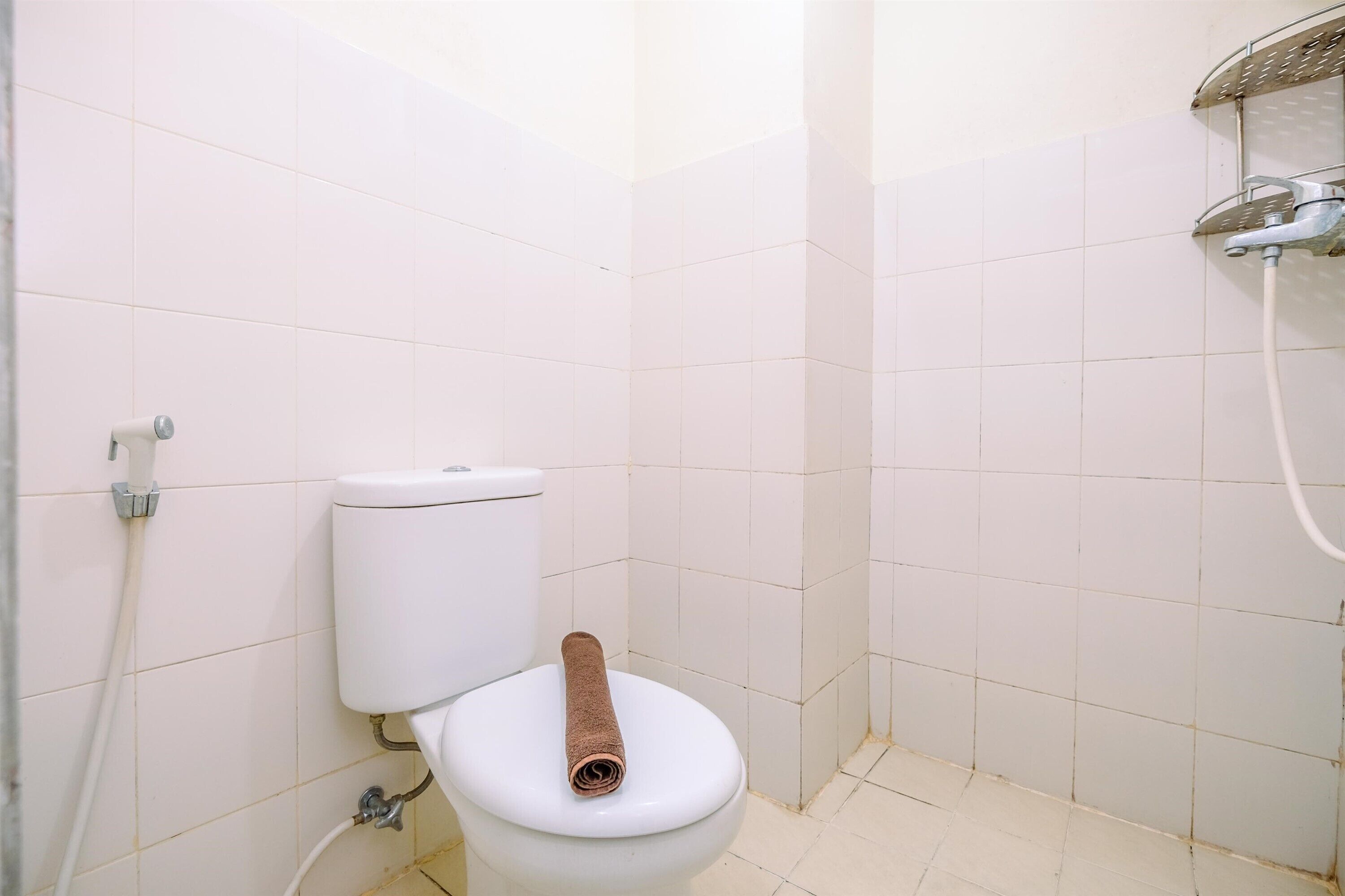 A small, clean bathroom with a toilet, a shower, and white tiled walls.