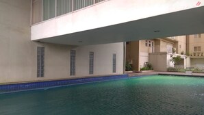 A swimming pool with a tiled edge, surrounded by a building with balconies and windows. - Spacious 3Br At Bogor Valley Apartment (Bogor)