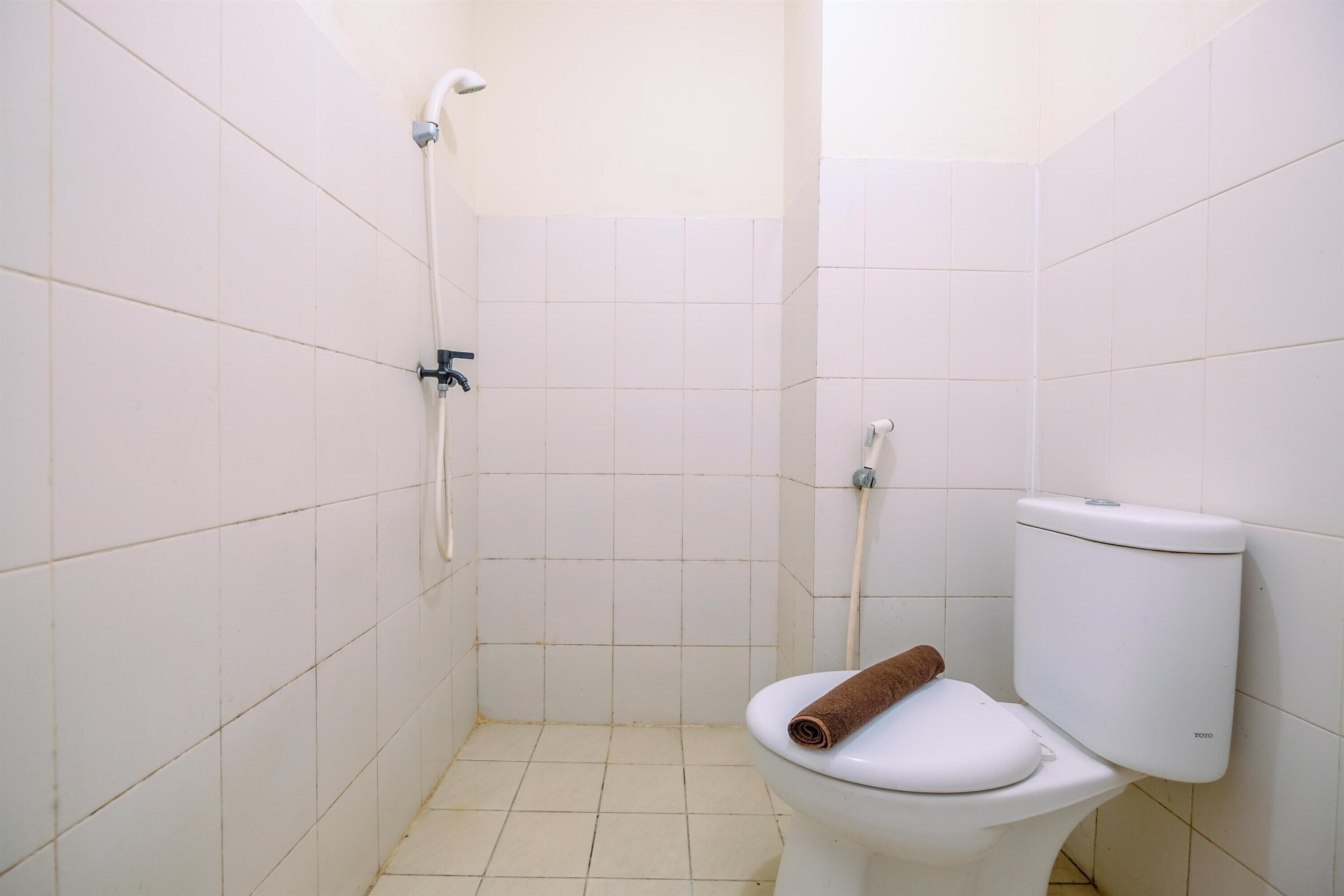 Een kleine badkamer met witte tegels, een toilet en een douche.