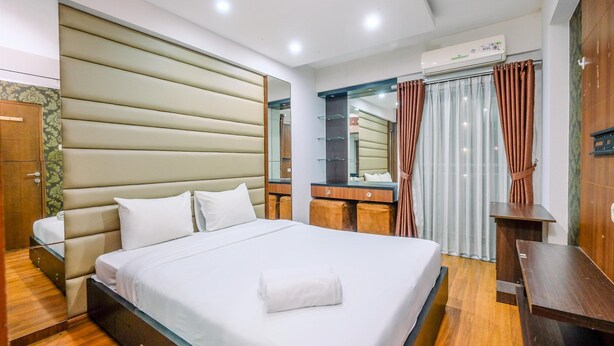 A modern hotel room with a large bed, wooden flooring, a built-in wardrobe, a bedside table, and a mirror. - Spacious 3Br At Bogor Valley Apartment (Bogor)