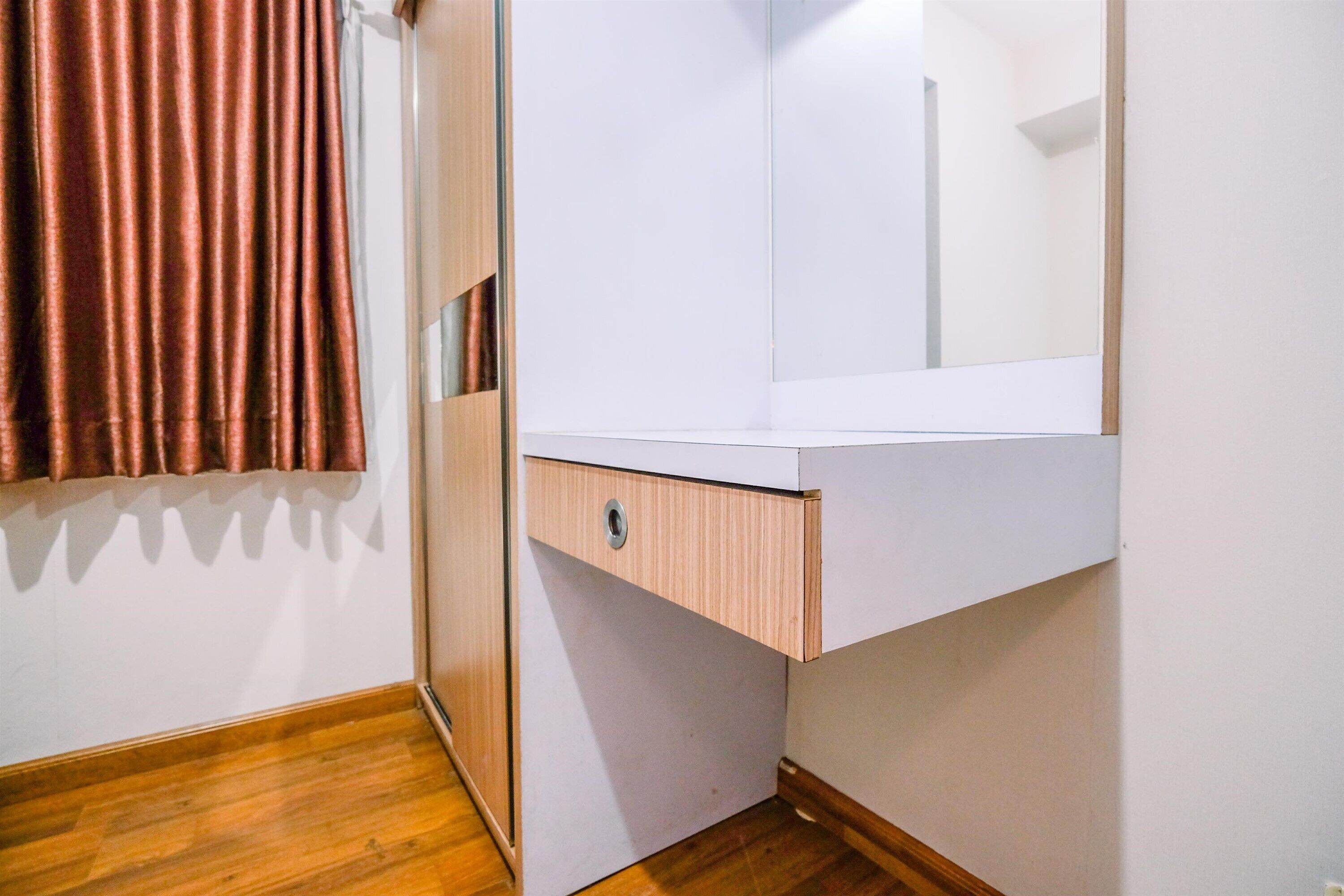A bathroom with a wooden floor, a white countertop, a mirror, and a brown curtain.