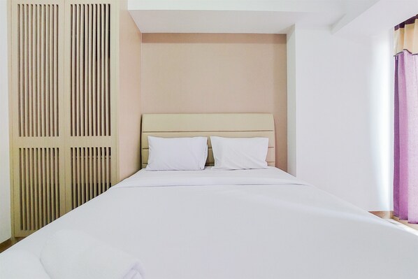 A single bed with white linens, a beige headboard, and a vertical slat vent on the left.