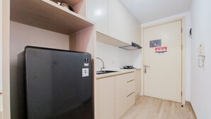 Una cocina compacta con un refrigerador negro, un lavamanos y una estufa. Hay una puerta con un letrero y un teléfono montado en la pared.