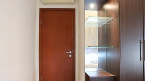A closed wooden door with a handle, a glass shelf unit with a mirror, and a small cabinet below it. - Full Furnished With Comfort Design 2Br Apartment At Thamrin Residence (Jakarta)