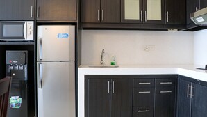 A kitchen with dark wood cabinets, a white countertop, a stainless steel refrigerator, a microwave, and a water dispenser. - Full Furnished With Comfort Design 2Br Apartment At Thamrin Residence (Jakarta)