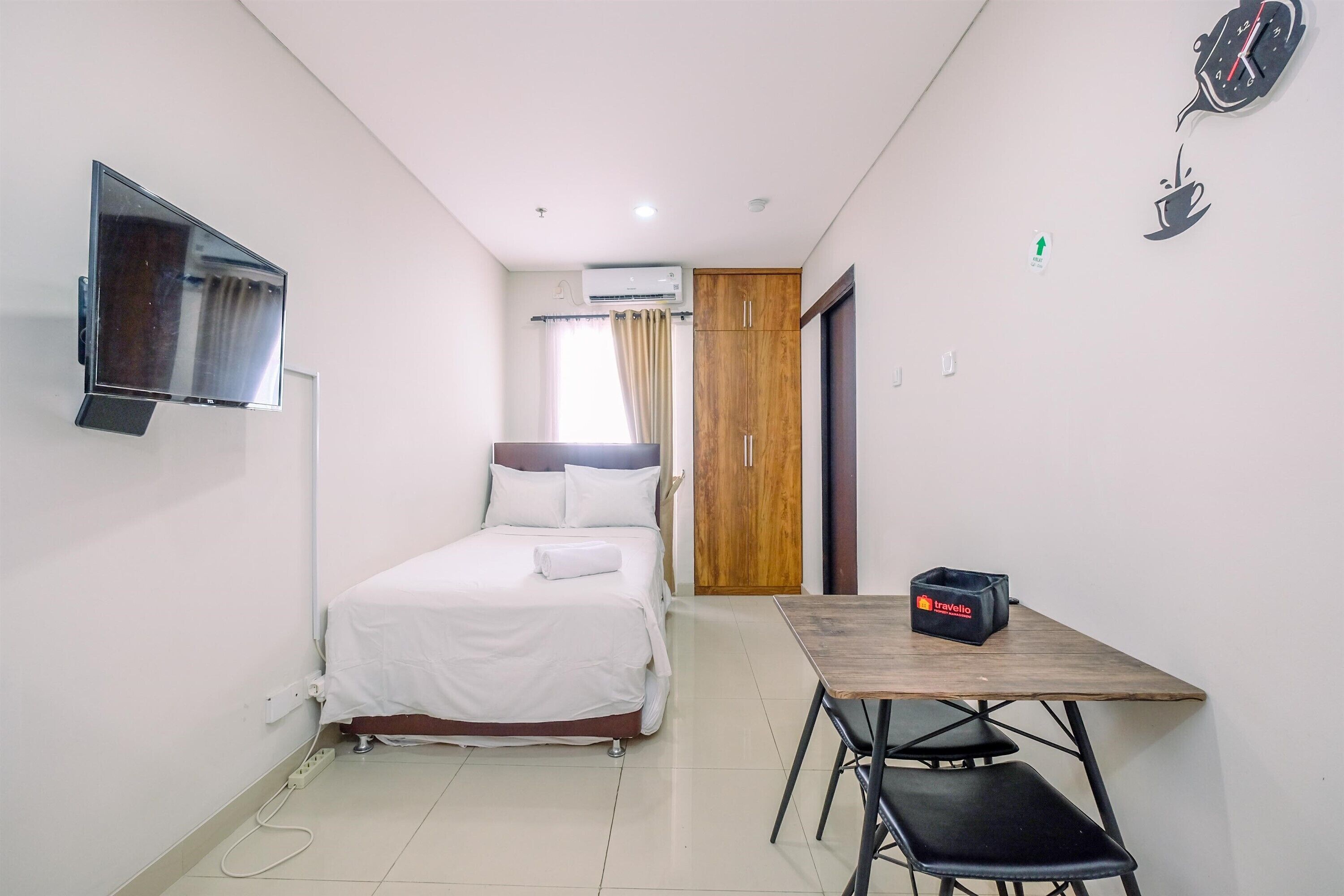 A compact hotel room with a bed, a TV mounted on the wall, a wooden table with a chair, and a wardrobe.