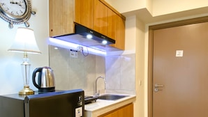 A compact kitchen with a refrigerator, a coffee maker, a sink, and wooden cabinets. - Homey And Modern 2Br At 6Th Floor Meikarta Apartment (Cikarang)