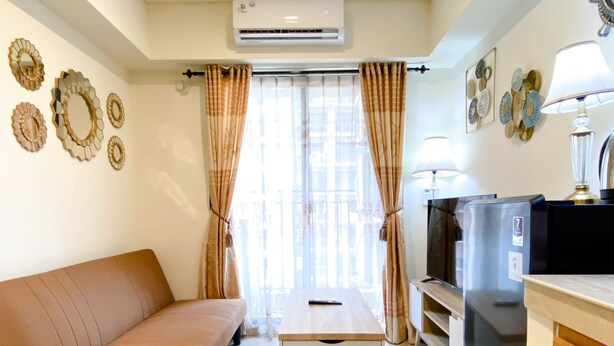 A compact living space with a sofa, a small table, a TV, and a refrigerator. - Homey And Modern 2Br At 6Th Floor Meikarta Apartment (Cikarang)