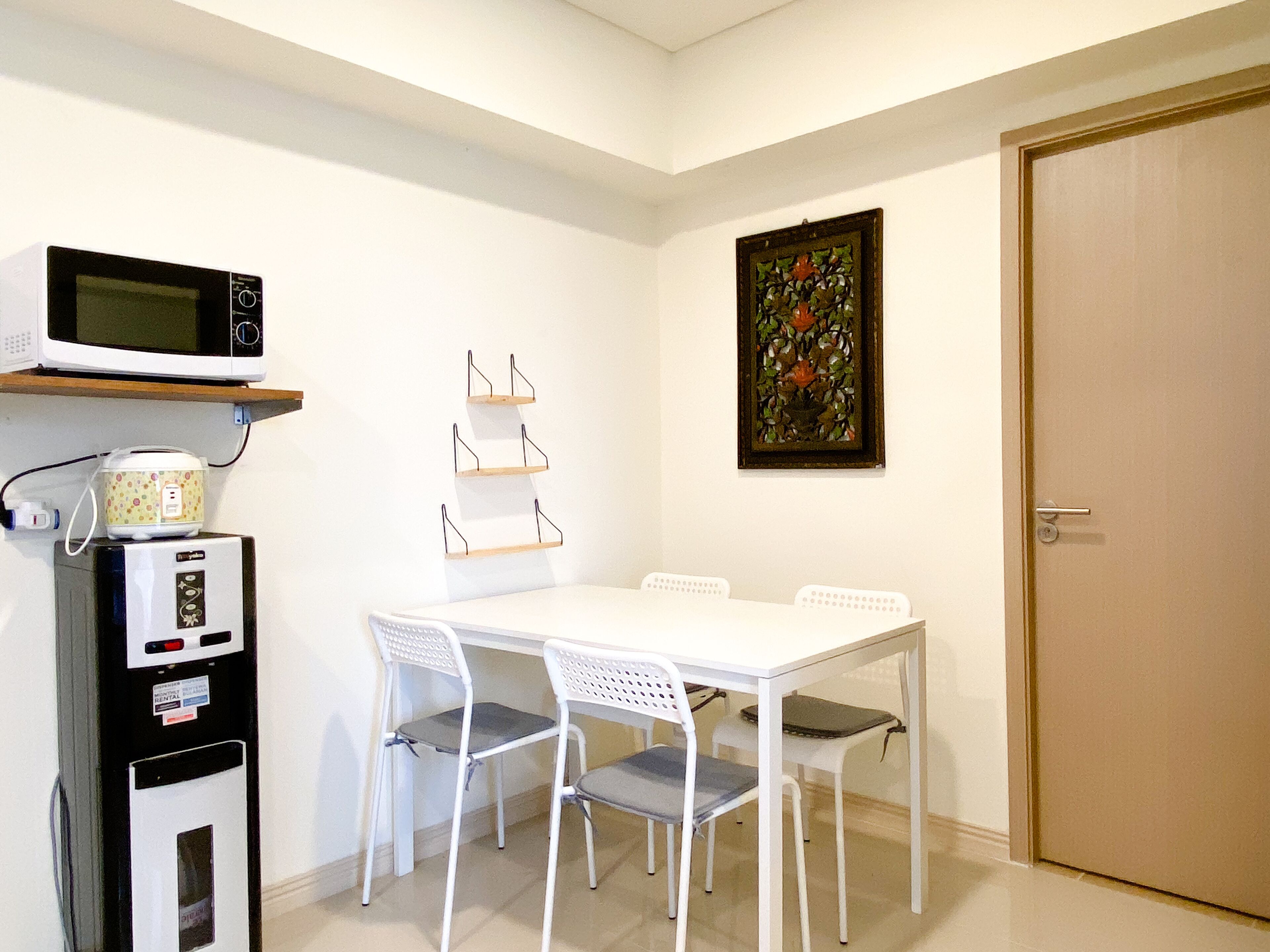 Una stanza piccola e pulita con un tavolo bianco e quattro sedie, un forno a microonde, un frigorifero e una porta.