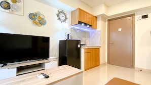 A compact kitchen with a TV, refrigerator, and wooden cabinets. - Homey And Modern 2Br At 6Th Floor Meikarta Apartment (Cikarang)