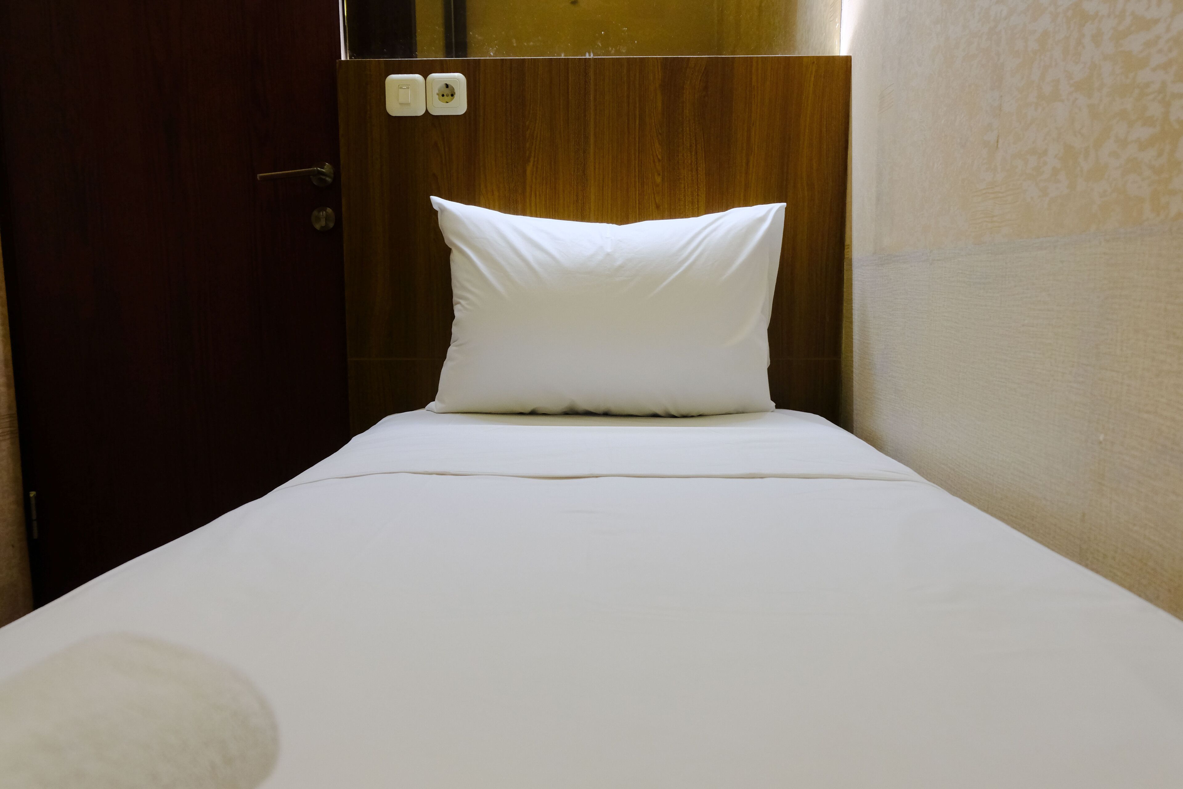 A single bed with a white pillow and a wooden headboard in a hotel room.