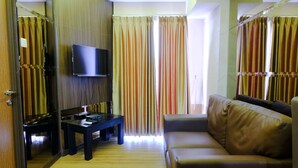 A hotel room with a wooden floor, a sofa, a TV, and curtains. - Strategic 2Br At Tamansari Panoramic Apartment (Bandung)
