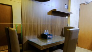 A small, modern room with a wooden wall, a glass table, and four leather chairs. There is a bottle of water and a box on the table. - Strategic 2Br At Tamansari Panoramic Apartment (Bandung)
