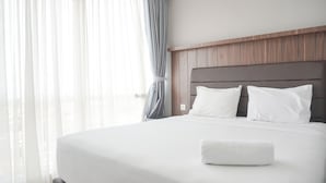 A neatly made bed with white linens and pillows, a wooden headboard, and sheer curtains on a window. - Modern Look And Comfy 2Br Menteng Park Apartment (Jakarta)