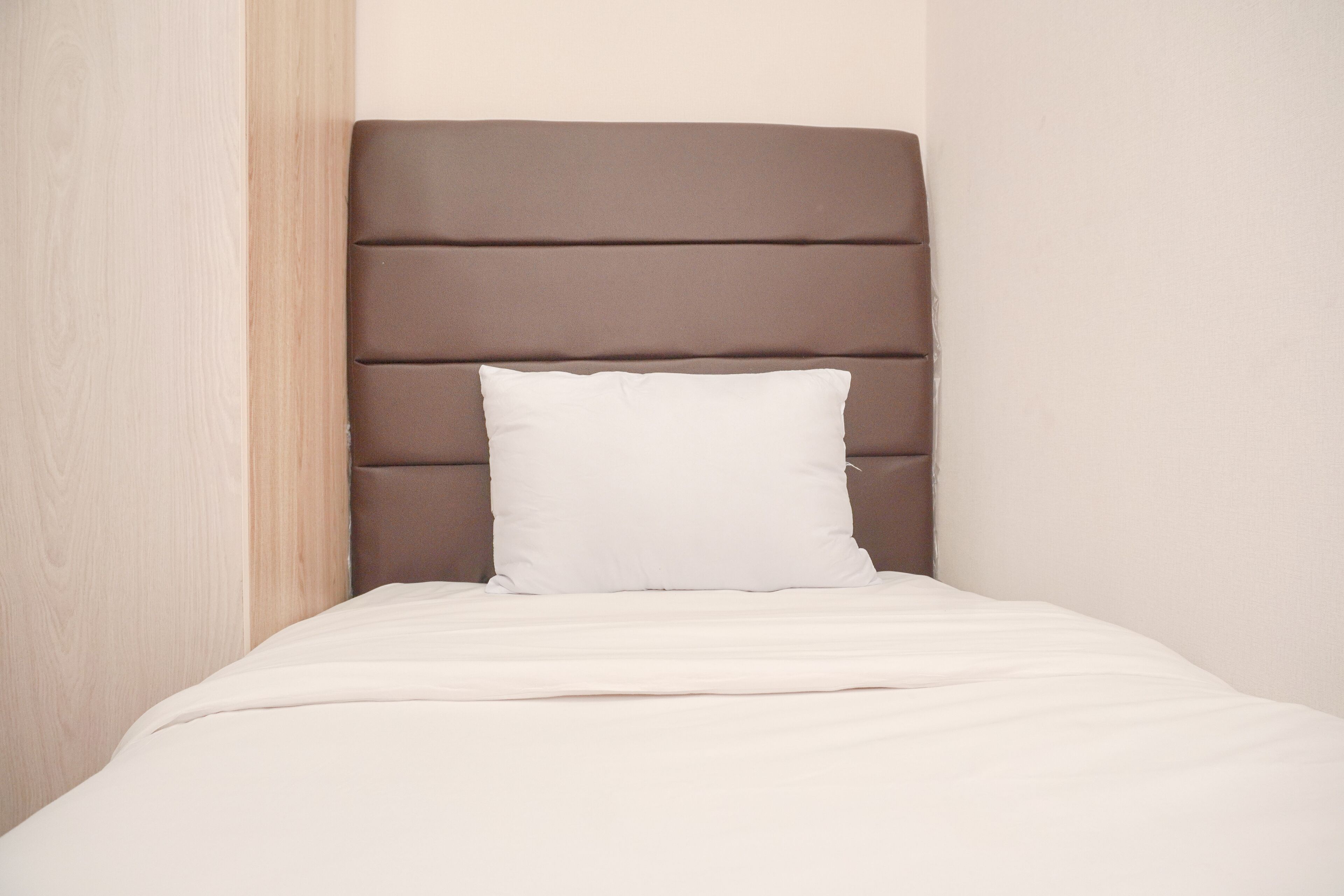 A neatly made bed with a brown headboard and a white pillow in a room with light-colored walls.