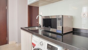 A compact kitchen with a microwave, a built-in washing machine, and a stainless steel sink. - Modern Look And Comfy 2Br Menteng Park Apartment (Jakarta)