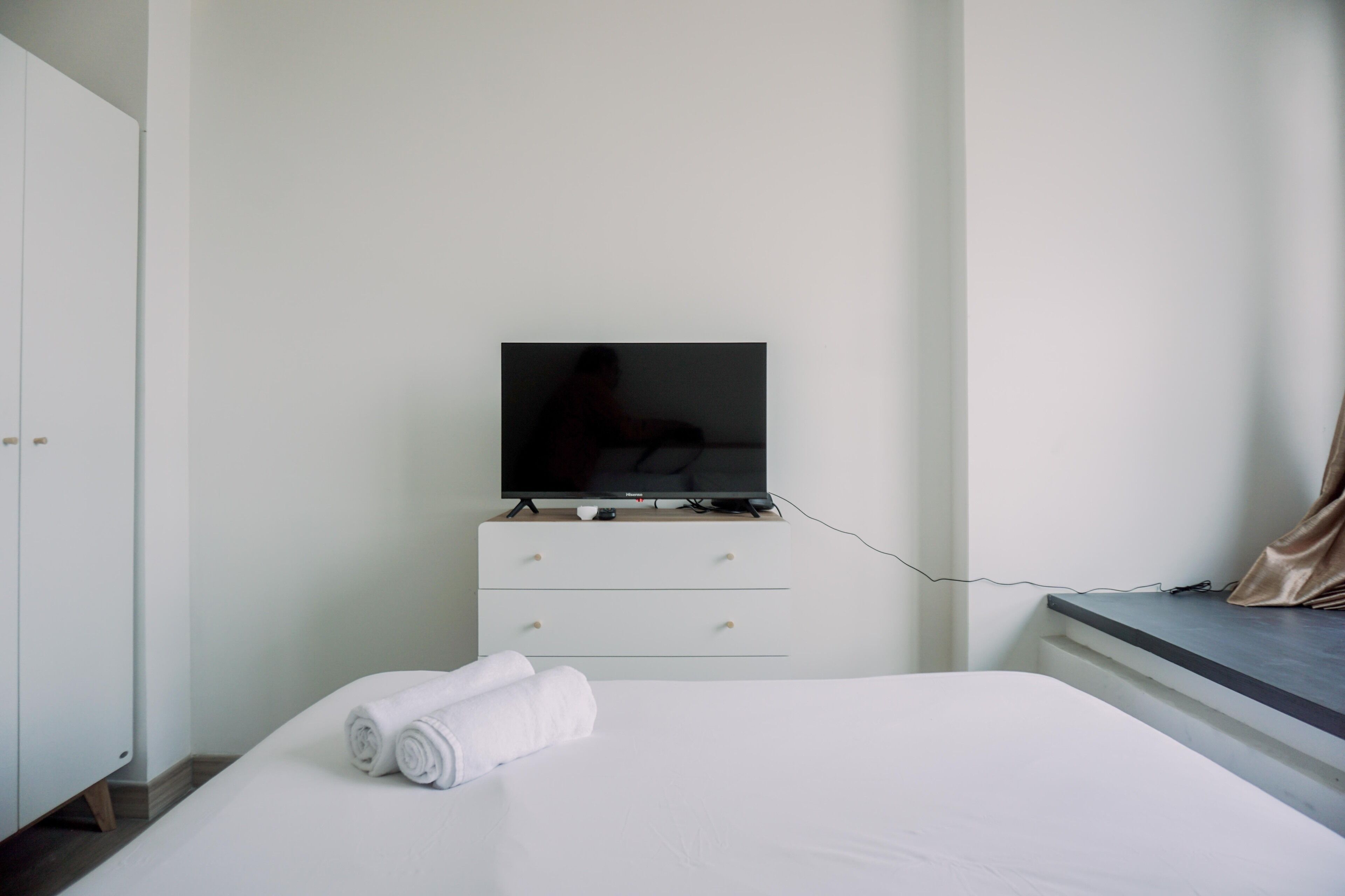 Une chambre d’hôtel avec un lit, un téléviseur posé sur une commode et une fenêtre avec des rideaux.