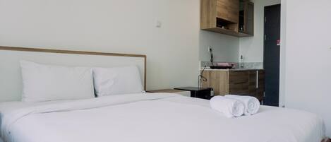 Una cama bien tendida con sábanas blancas y toallas enrolladas, un cabecero de madera y una mesita de noche con una lámpara.