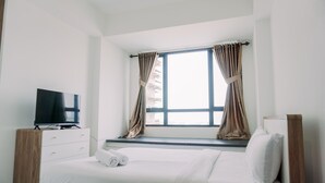 A bedroom with a bed, a TV, a window with curtains, and a wooden nightstand.