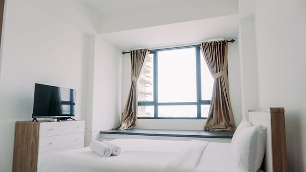 Ein Schlafzimmer mit einem Bett, einem Fernseher, einem Fenster mit Vorhängen und einem Nachttisch aus Holz.