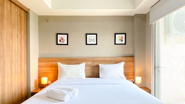 A hotel room with a large bed, two bedside lamps, and three framed pictures on the wall. - Big Studio At Apartment Mustika Golf Residence (Cikarang)