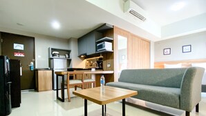 A modern living room with a grey sofa, wooden coffee table, and a kitchen area with a fridge, microwave, and cabinets.