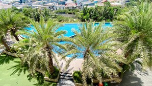 A swimming pool surrounded by palm trees, with a view of a residential area in the background. - Big Studio At Apartment Mustika Golf Residence (Cikarang)