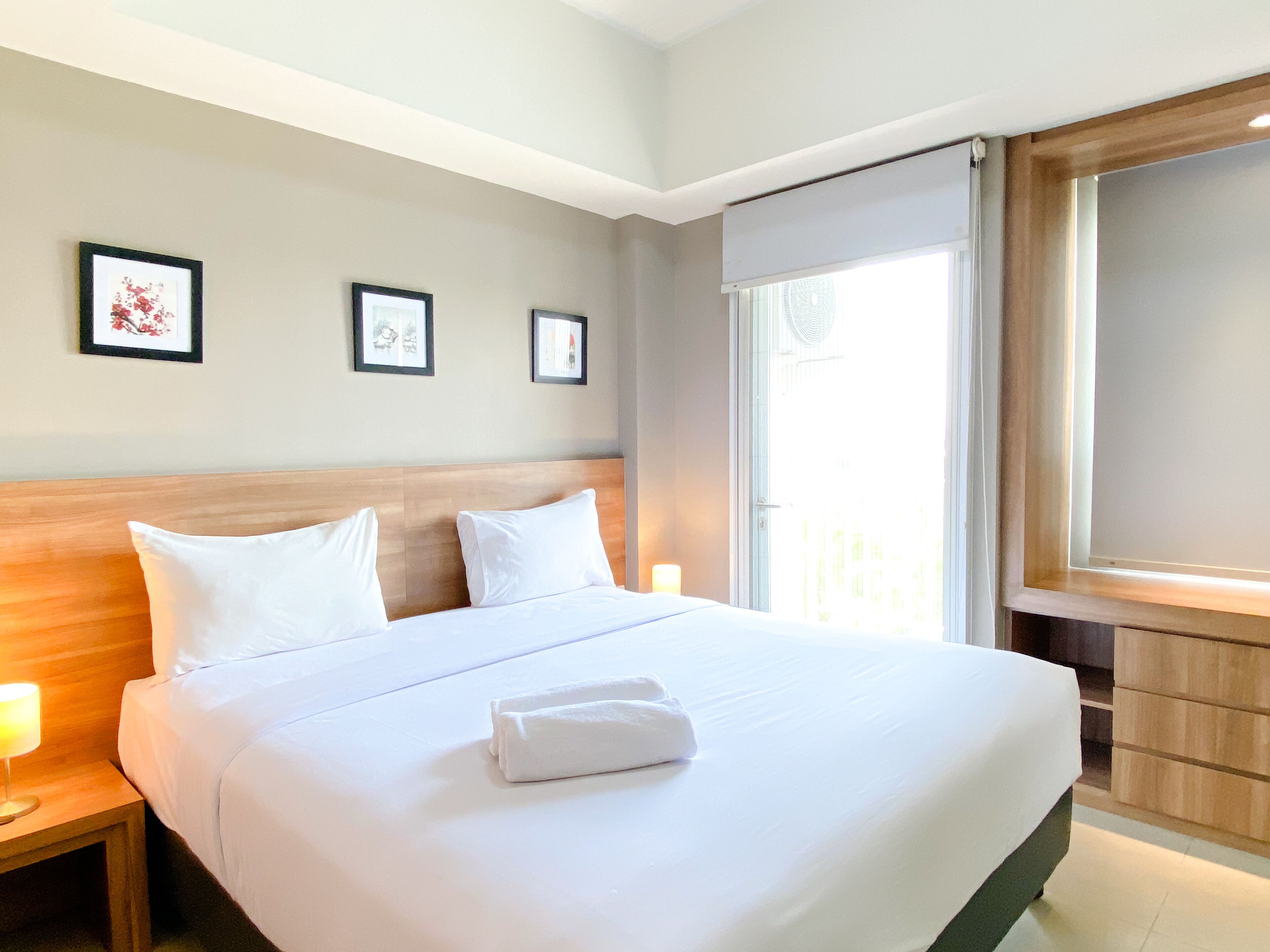 A hotel room with a large bed, wooden headboard, white bedding, and framed pictures on the wall.