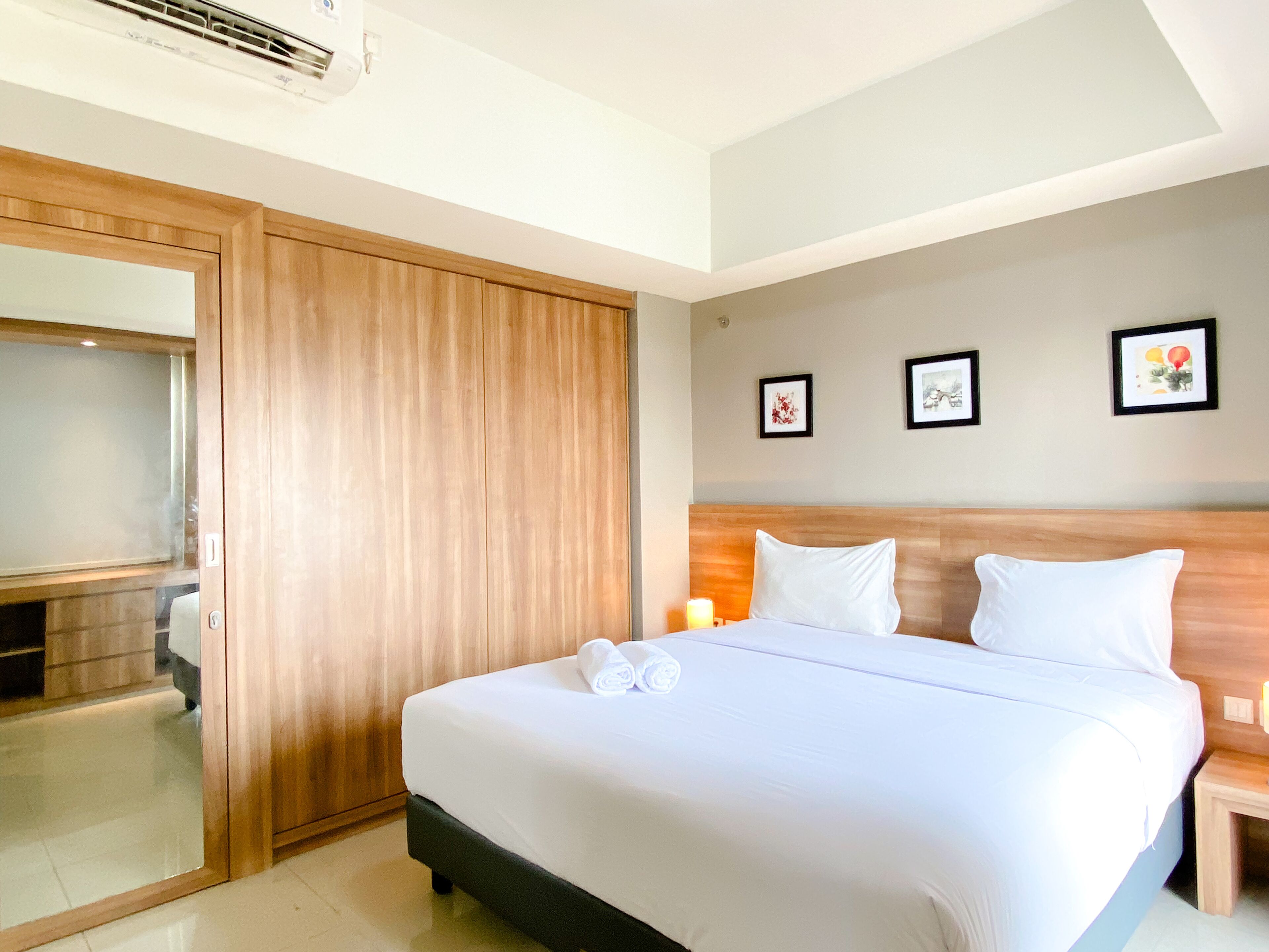A hotel room with a bed, a wooden wardrobe, a mirror, and three framed pictures on the wall.