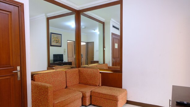 A room with a sectional sofa, a wooden door, and a large mirror reflecting the room. - Scenic 2Br At Grand Setiabudi Apartment (Bandung)