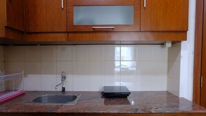 A kitchen with wooden cabinets, a granite countertop, a stainless steel sink, and a small black appliance. - Scenic 2Br At Grand Setiabudi Apartment (Bandung)