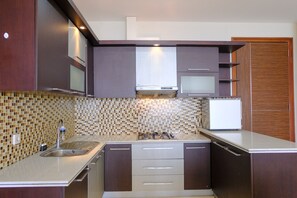 A modern kitchen with a gas stove, stainless steel sink, and wooden cabinets. - Spacious Designed 2Br Dago Butik Apartment (Bandung)