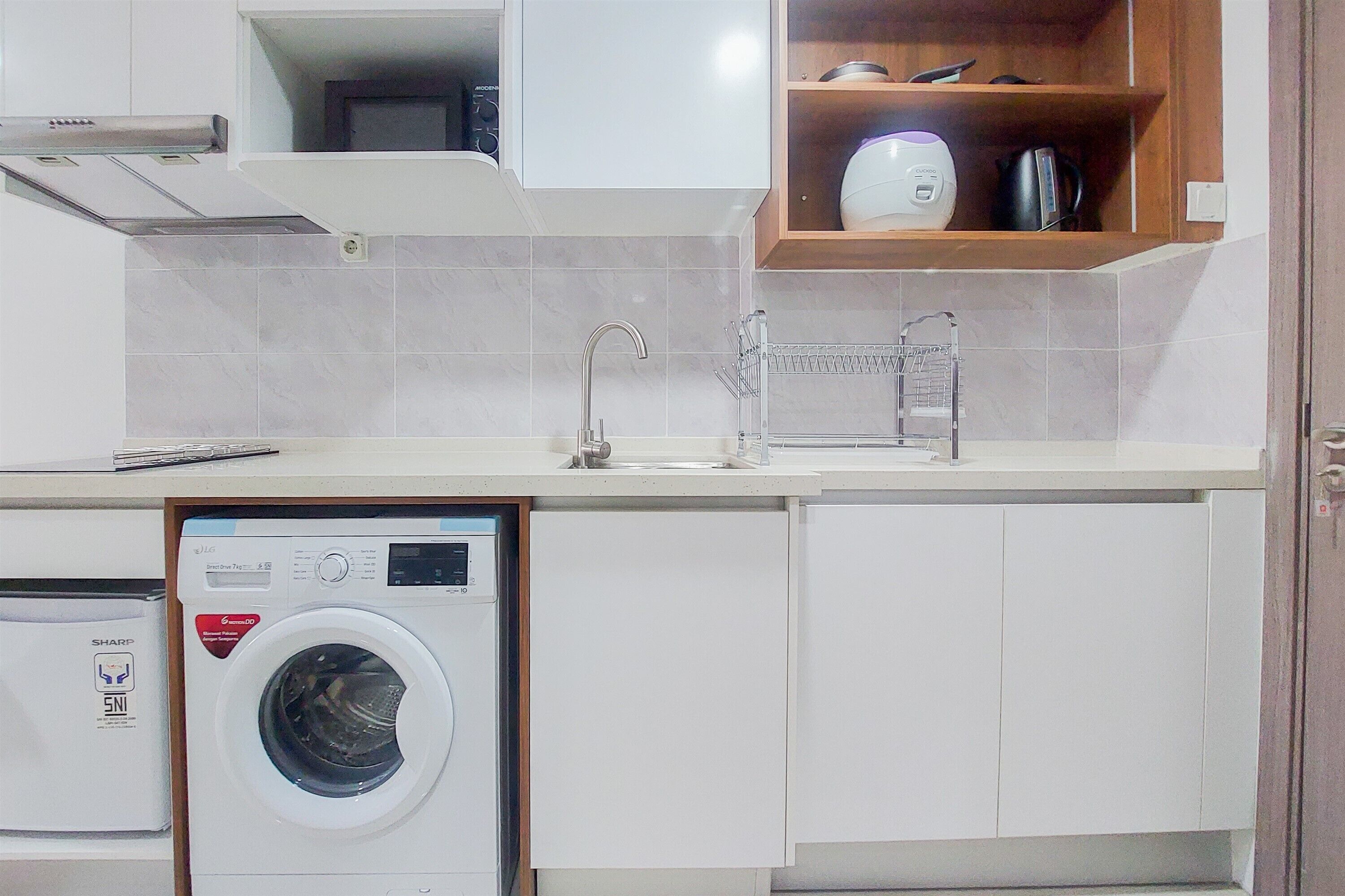 Une cuisine compacte équipée d’un lave-linge intégré, d’un évier avec un robinet et d’une étagère en bois au-dessus de l’évier.