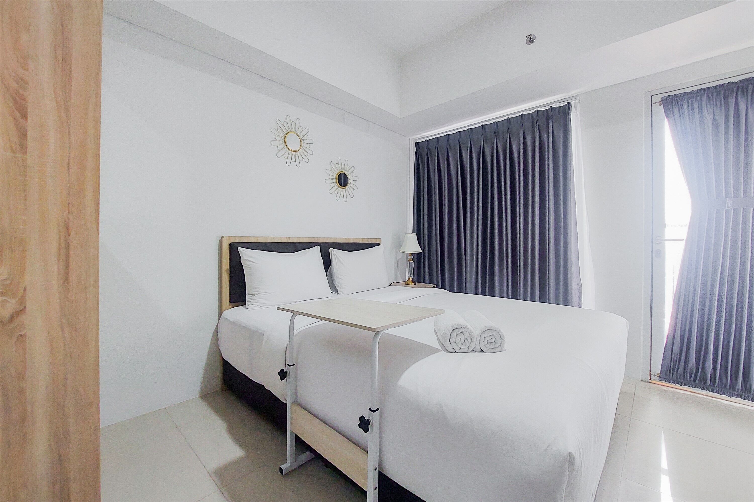 A hotel room with a bed, a bedside table, a lamp, and curtains.