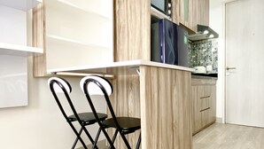 A compact kitchen with a built-in microwave, a small refrigerator, and a wooden cabinet. There are two black chairs with a metal frame. - Homey And Compact Studio At Azalea Suites Apartment (Cikarang)
