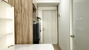 A narrow hallway with a wooden cabinet on the left, a white door at the end, and a white door on the right. - Homey And Compact Studio At Azalea Suites Apartment (Cikarang)