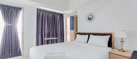 A hotel room with a large bed, a bedside table with a lamp, and a view of the outside through a window with curtains.