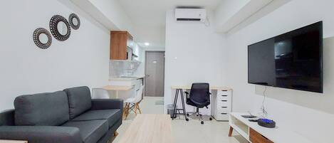 Una sala de estar moderna con un sofá negro, una mesa de centro de madera, un televisor y un escritorio con una silla.