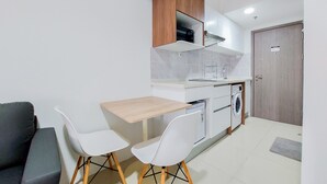 A compact kitchen with a wooden cabinet, a washing machine, and a small dining area with two chairs. - Homey Living Studio Tamansari Bintaro Mansion Apartment (South Tangerang)
