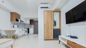 A modern kitchen with a microwave, oven, and washing machine. There's a dining area with a table and chairs, and a TV mounted on the wall. - Homey And Cozy Stay 1Br Tamansari Bintaro Mansion Apartment (South Tangerang)