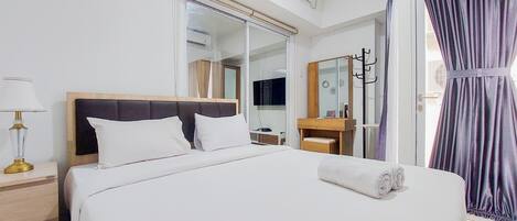 A hotel room with a bed, a nightstand, a lamp, a mirror, a vanity, and a window with curtains.
