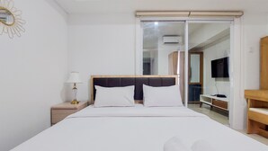 A neatly made bed with white linens and pillows, a bedside lamp, and a wooden nightstand. - Homey And Cozy Stay 1Br Tamansari Bintaro Mansion Apartment (South Tangerang)