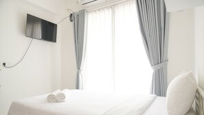 Una habitació d'hotel amb un llit, un televisor de pantalla plana al mur i una finestra amb cortines.
