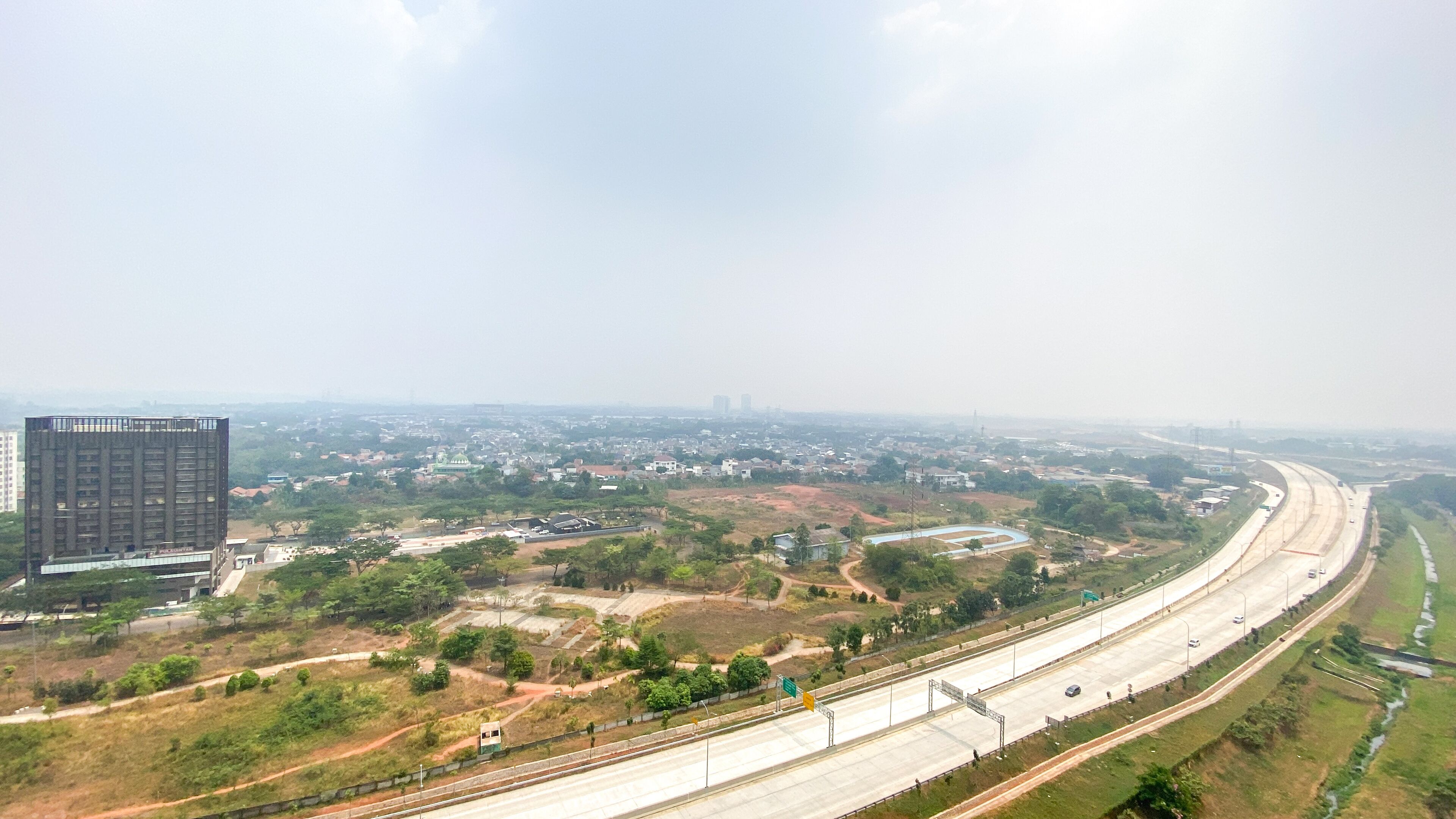 A highway with multiple lanes, a large building on the left, and a distant cityscape.
