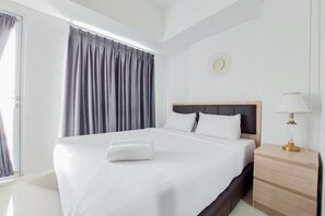 A hotel room with a large bed, a bedside table with a lamp, and a window with curtains. - Simply Look And Comfort 1Br Tamansari Bintaro Mansion Apartment (South Tangerang)