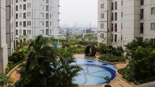 A residential building with a swimming pool surrounded by greenery. - Best Deal And Well Furnished 2Br Bassura City Apartment (Jakarta)