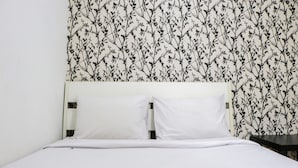 A bed with white bedding and a floral wallpaper pattern on the wall behind it. - Best Deal And Well Furnished 2Br Bassura City Apartment (Jakarta)