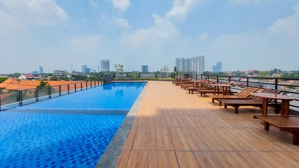 A rooftop pool with wooden deck and lounge chairs, overlooking a cityscape.